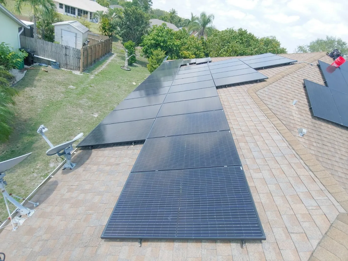 Aerial view of black solar panels on a shingle roof beside satellite dishes